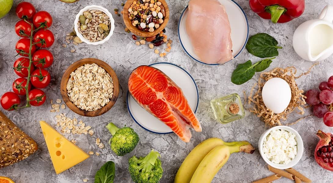 Różne produkty na stole będące źródłem witaminy B6 np. łosoś, mięso, banan, płatki owsiane